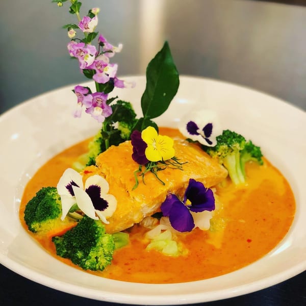 Siam Nara Thai Cuisine's salmon in red curry with broccoli, garnished with edible flowers.