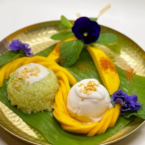 Thai mango sticky rice with green rice, coconut ice cream, and fresh mango slices on a gold plate.