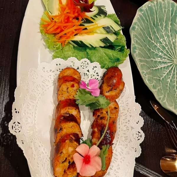 Thai sausage slices with fresh lettuce, shredded carrots, and carved cucumber on a white plate.