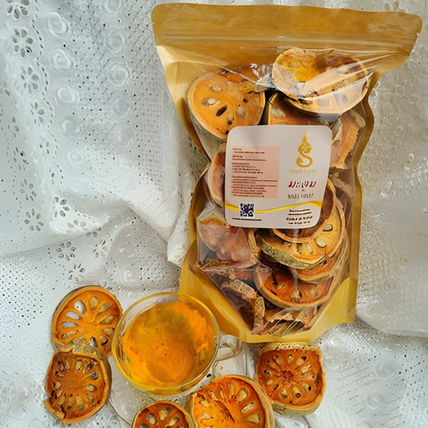 Dried bael fruit slices in a clear bag and scattered, with a cup of bael tea.