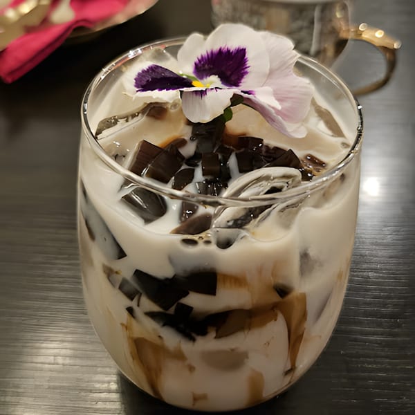 Thai iced tea with grass jelly and a purple edible flower on top.