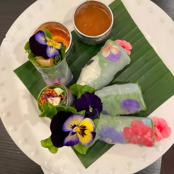 Fresh spring rolls with edible flowers and two dipping sauces on a banana leaf.