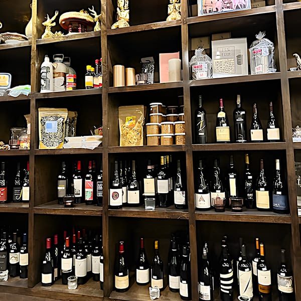 A dark wooden shelving unit filled with various bottles of wine, decorative items, and packaged goods.