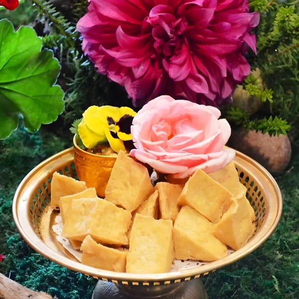 Golden fried tofu pieces in a decorative bowl, surrounded by pink and yellow flowers and greenery.