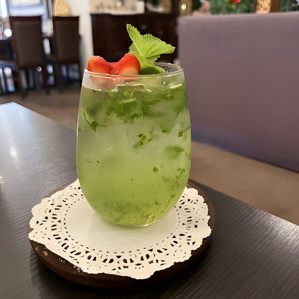 A green Thai iced drink with mint and strawberry garnish sits on a doily.