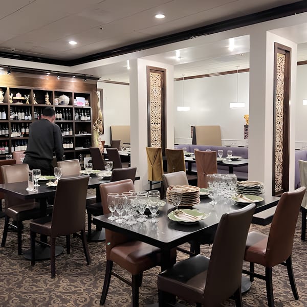 A server arranges tables in the elegant dining room of Siam Nara Thai Cuisine, featuring a wine wall and ornate decor.