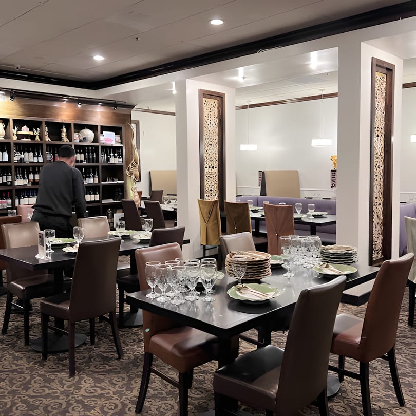 A server arranges tables in the elegant dining room of Siam Nara Thai Cuisine, featuring a wine wall and ornate decor.
